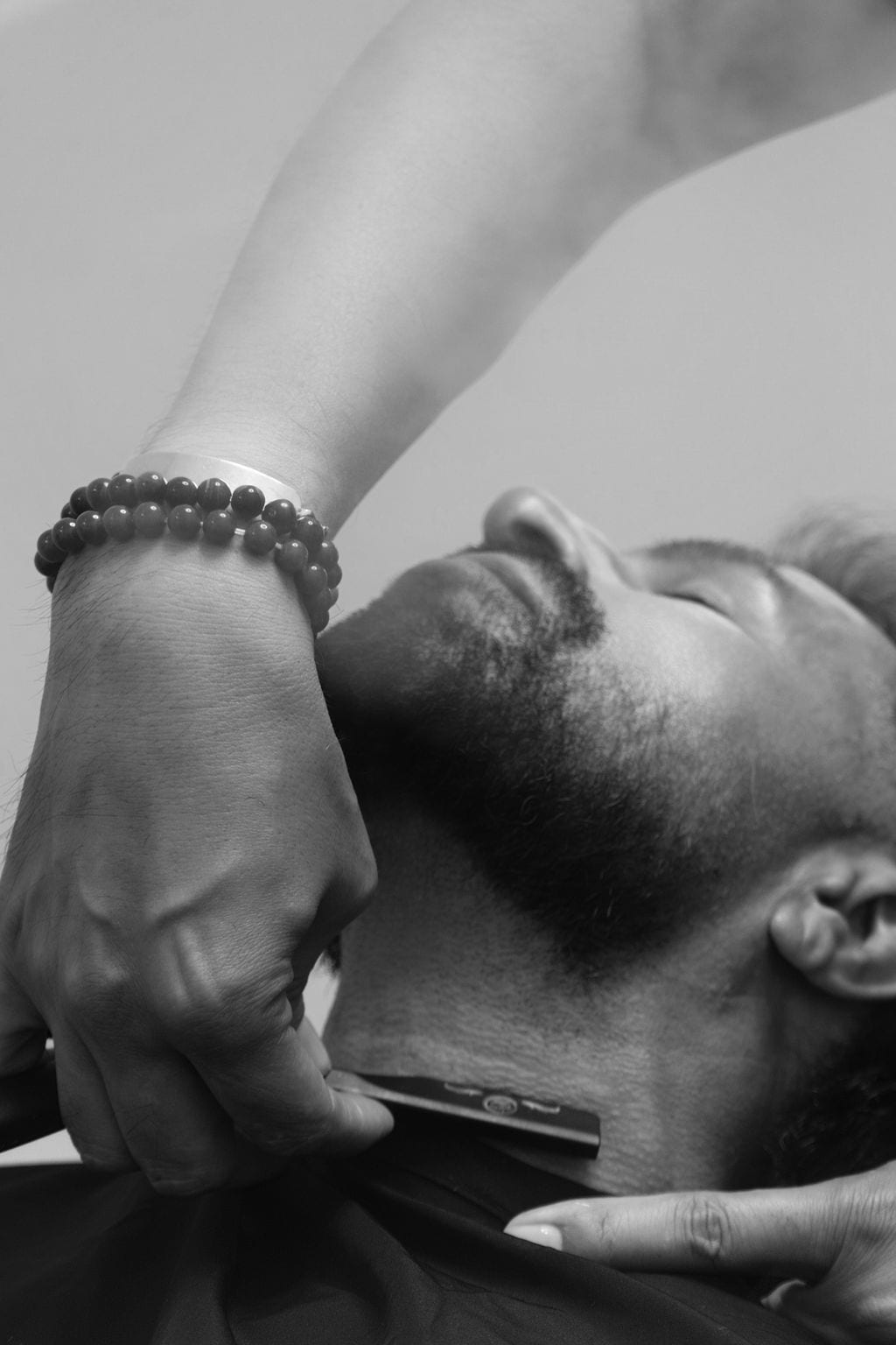Black and white detail of a neckline being defined, hand and razor against the throat