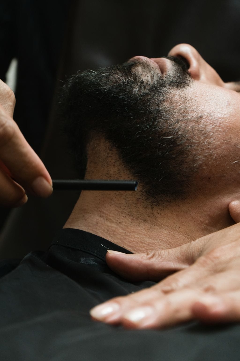Close detail of a neckline being defined with a straight razor along the beard