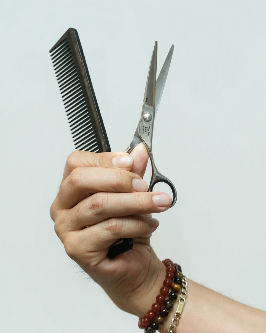 A raised hand holding a comb and scissors against a light wall